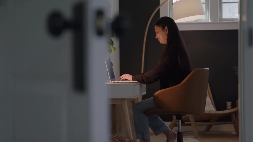 Woman sits at a table typing on a laptop computer