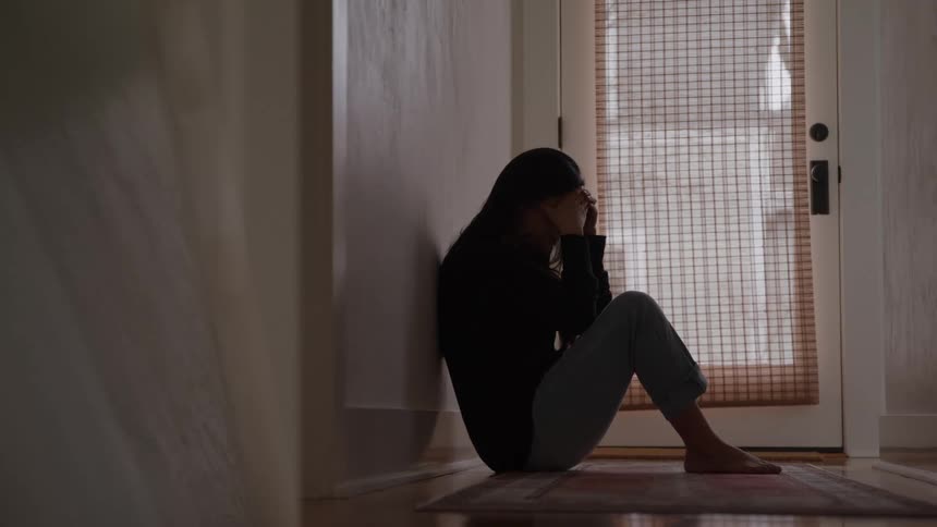 A woman sitting on the floor of a room with her hands on her head with a sad expression