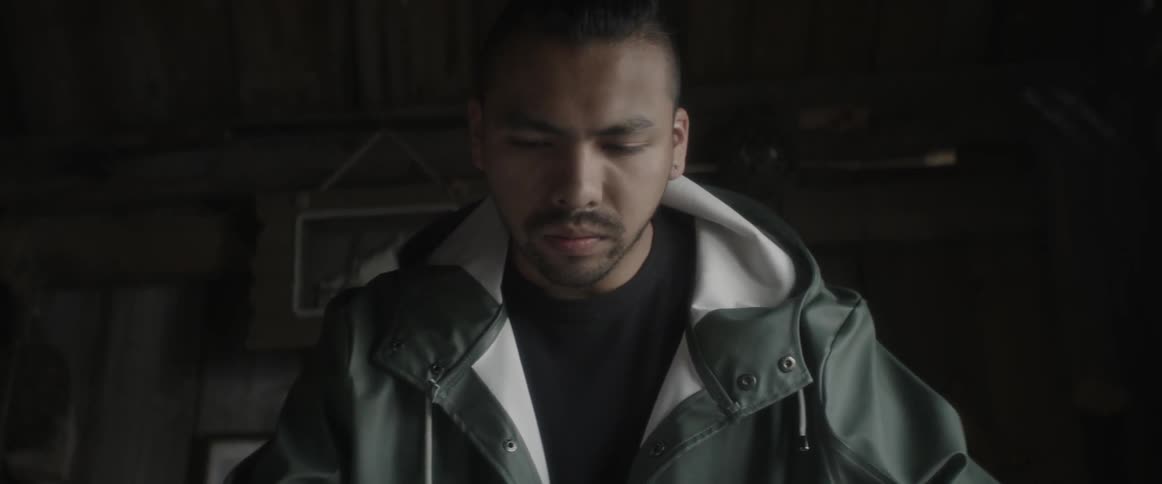Man in a green jacket looking down at something indoors
