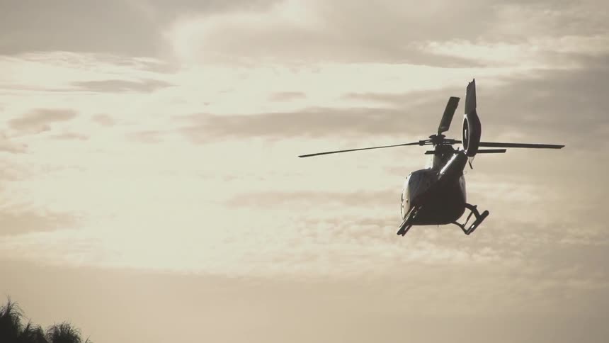 A helicopter flies across a cloudy sky