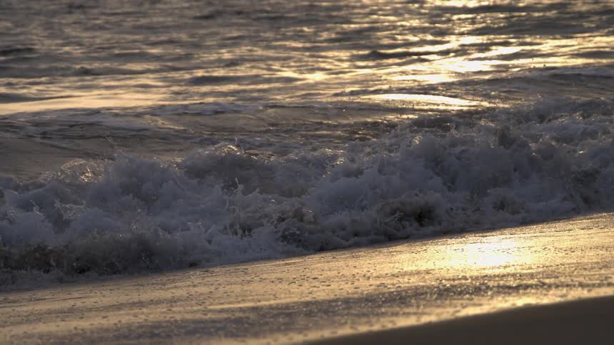 Sunlight shines on the coast as waves roll into shore and over the beach