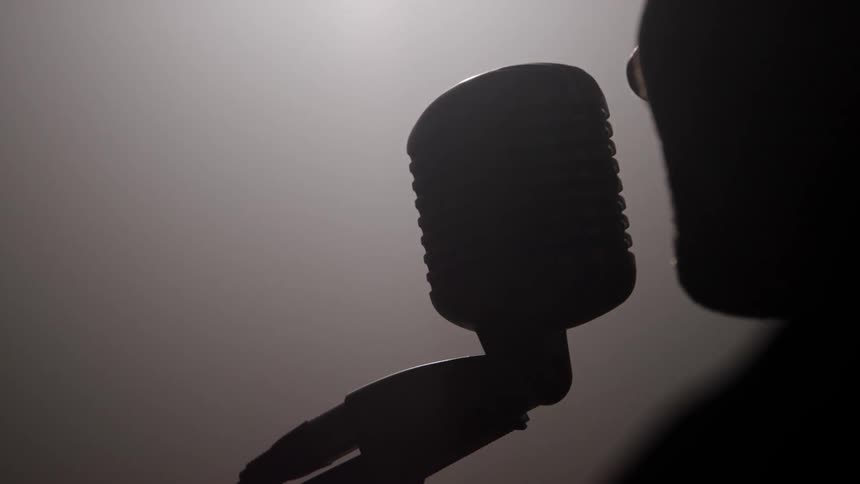 Musician on stage speaks into a microphone in a dark smoke filled room