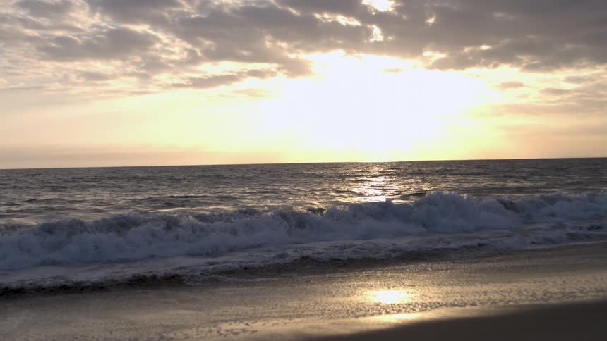 Waves gently crash on the sand under the golden glow of the sunset