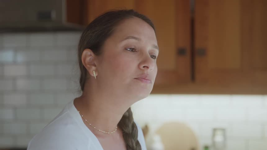 Woman standing in her kitchen stares into space briefly