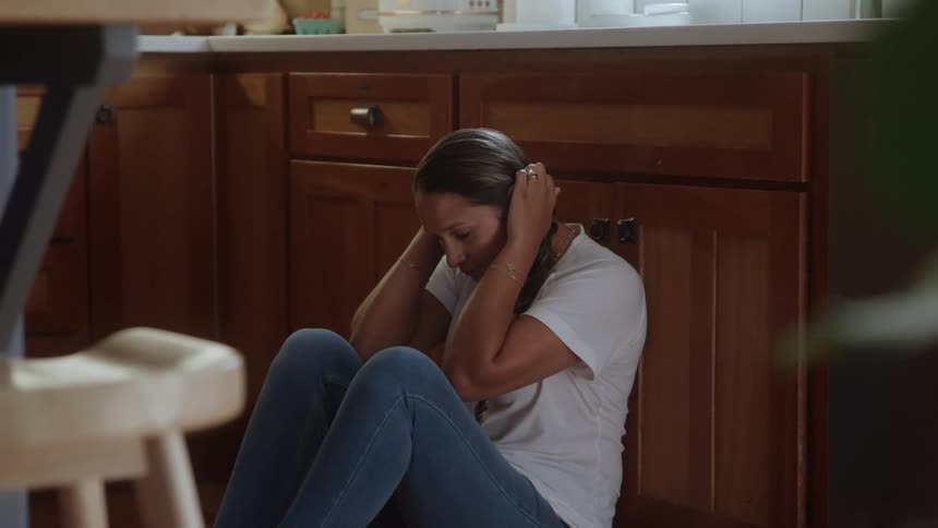 Woman sitting on the kitchen floor rubbing her face and head with her hands