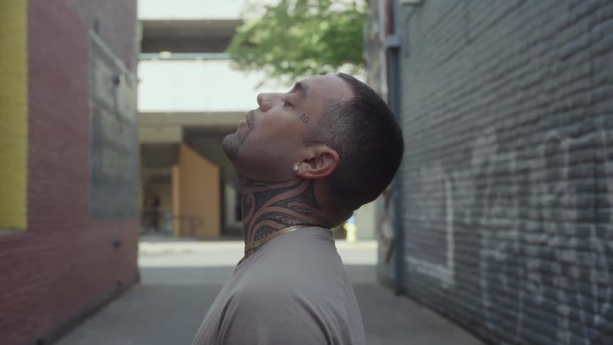 A man tilts his head back while standing in a narrow urban alley