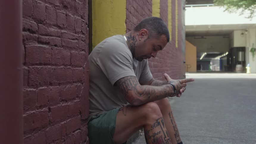 Man sitting on the stoop of a building with his head down and hands together as he thinks