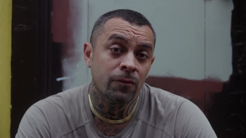 The face of a man with short hair and wearing a gold necklace staring straight ahead
