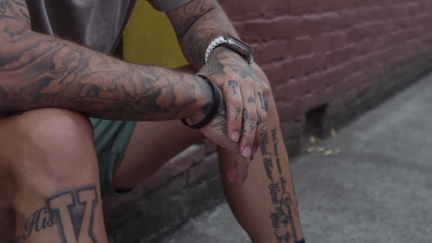 Man with several tattoos sits on a stoop during the daytime