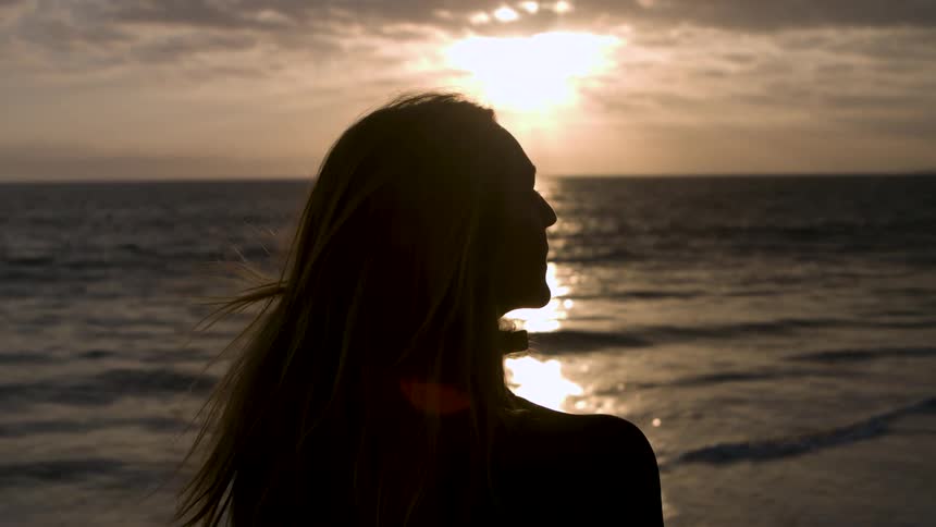 Woman stands on the beach looking around while the sun shines from a red sky