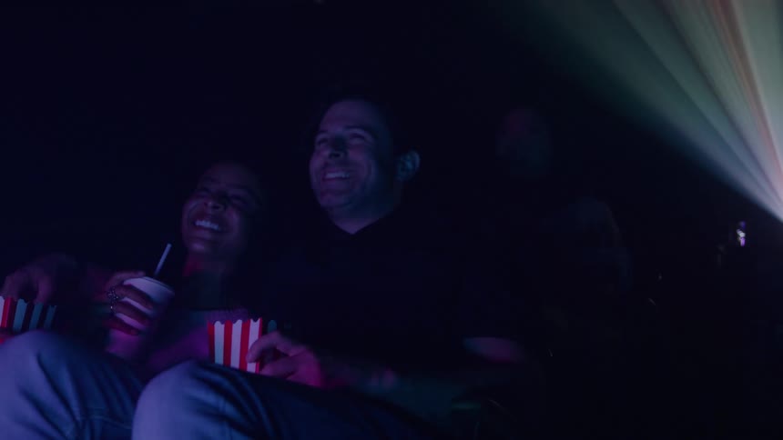 A couple laughs together while watching a movie in a dark theater