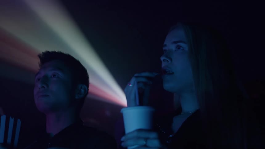 Two people in a theater snack on popcorn while watching a movie