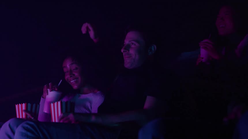 The man puts his arm around a womans shoulders in the movie theater