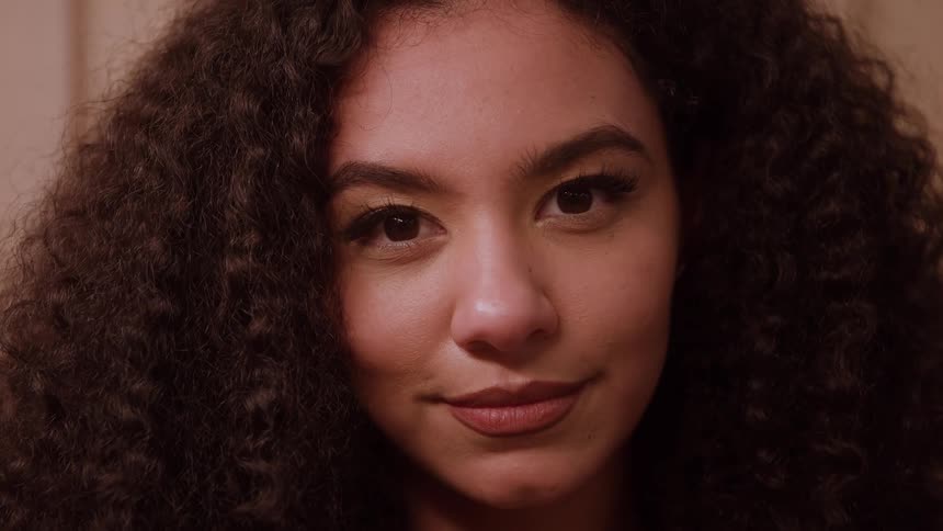 An extreme closeup shot captures a woman with curly hair turning from profile to look directly at the camera