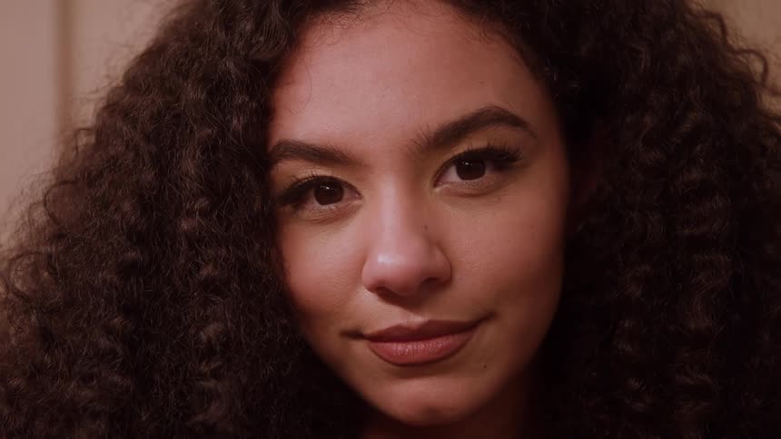 The face of a young woman with a subtle smile and curly hair looking forward