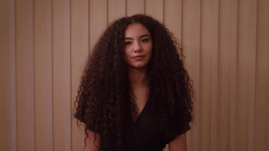 A medium shot shows a woman with long voluminous curly hair opening her eyes to look at the camera