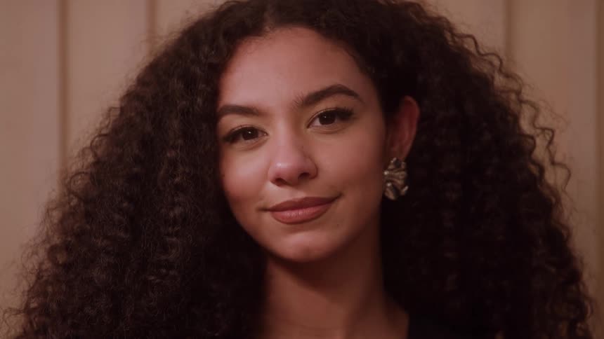 A closeup portrait shows a young woman with long curly hair looking offcamera before turning to smile