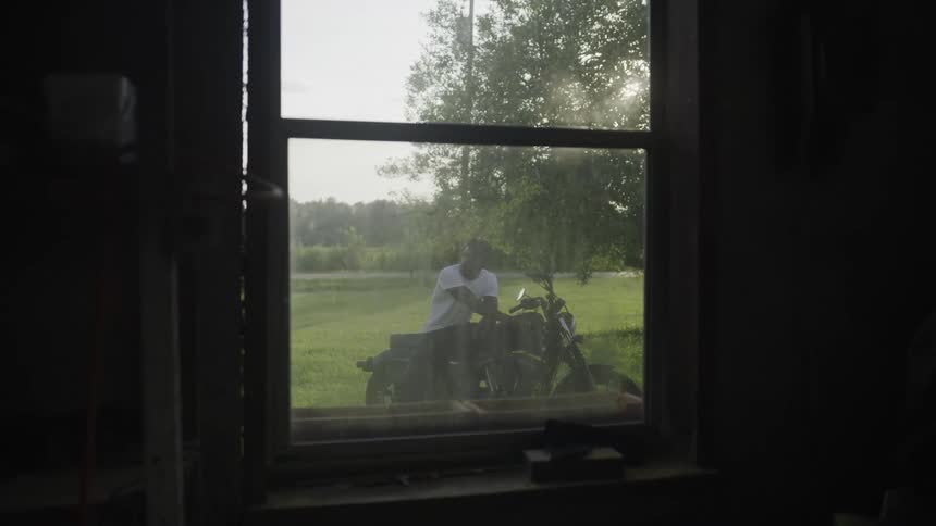 A man is sitting on his motorcycle outside the dark rooms window