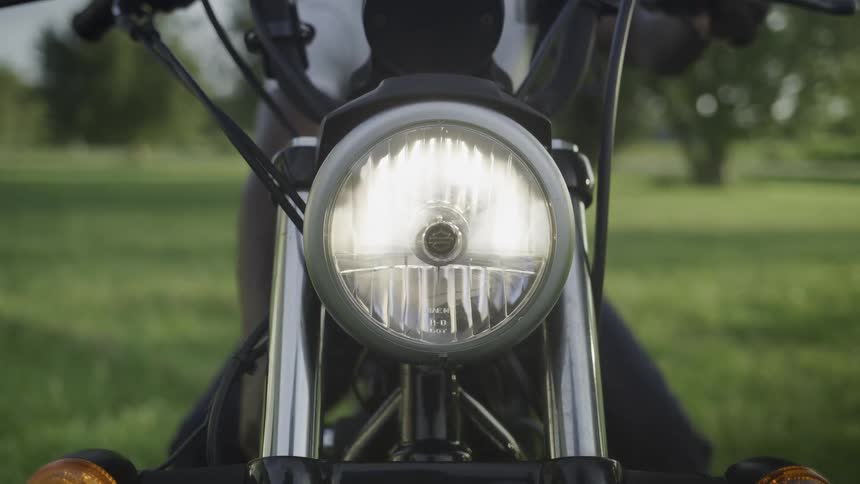 Man sitting on a motorcycle in a field turns it on and the headlight comes on