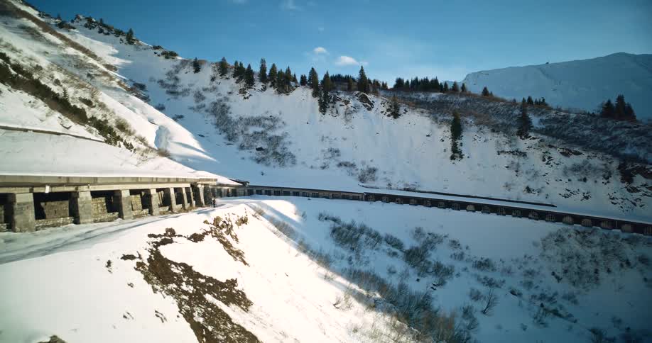 Aerial view of a snowy mountain road the camera flies past an empty covered section of the roadway