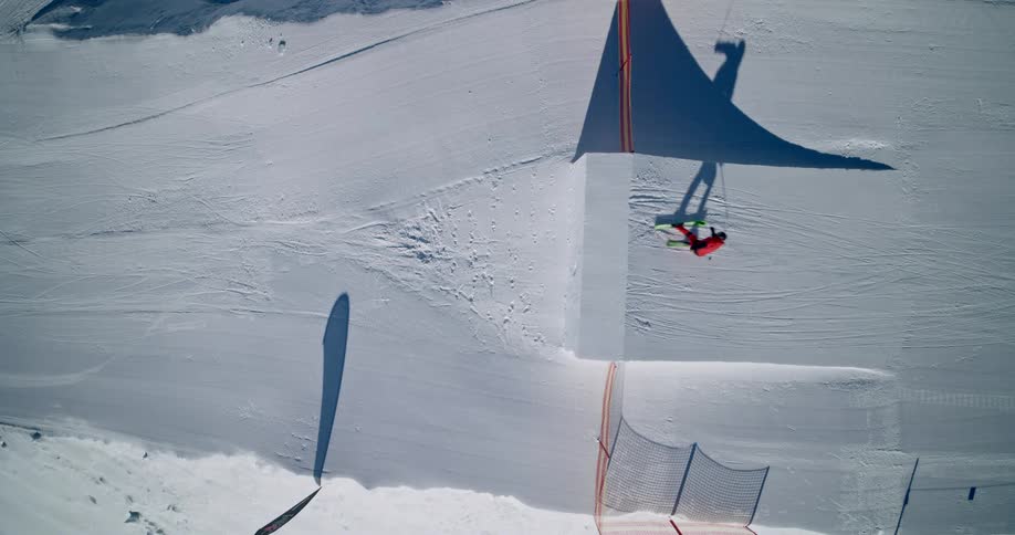 Steady top shot of a Skier jumping off a ramp on a snowcovered slope under bright sunlight