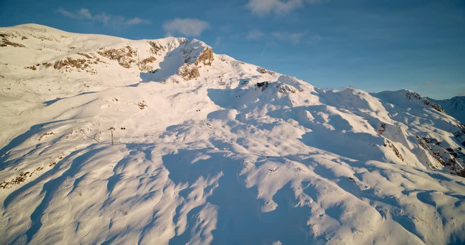 Aerial of a large snow covered mountain on a clear blue day with clouds in the sky