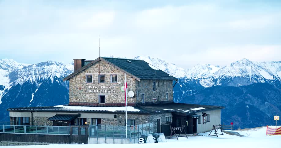 A stone lodge the patscherkofel schutzhaus sits on a snowy mountain top with a vast snowcovered mountain range behind it