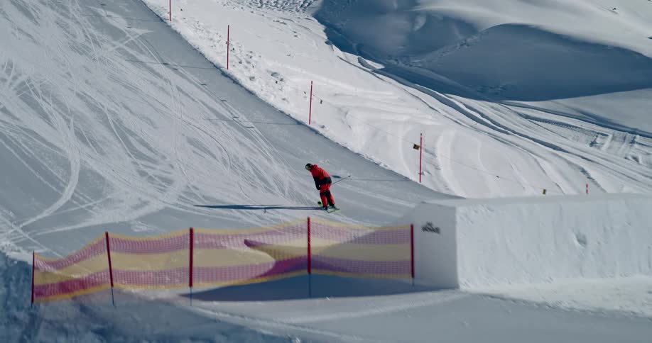 Person skiing backwards on a snowy slope takes a ramp and performs a jump trick