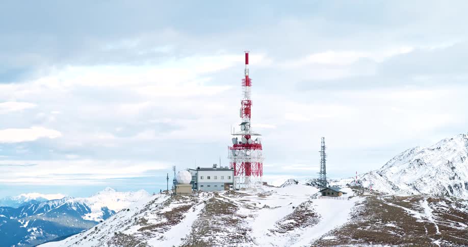 An aerial view of a snowy mountain peak which is home to a transmission tower