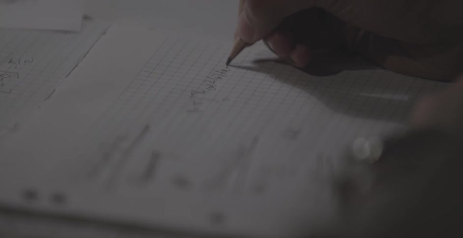 Person writes equations on a piece of graph paper with a pencil