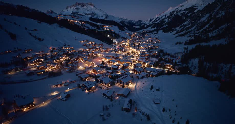 Aerial of fairytale-like alpine village with lights on houses glowing in a mountain valley