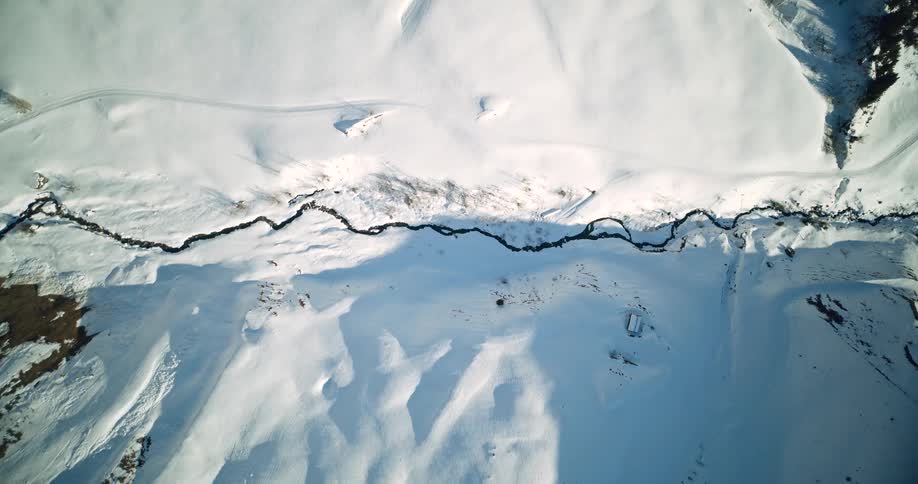 Top shot of winding river cuts through the snowcovered valley seen from above