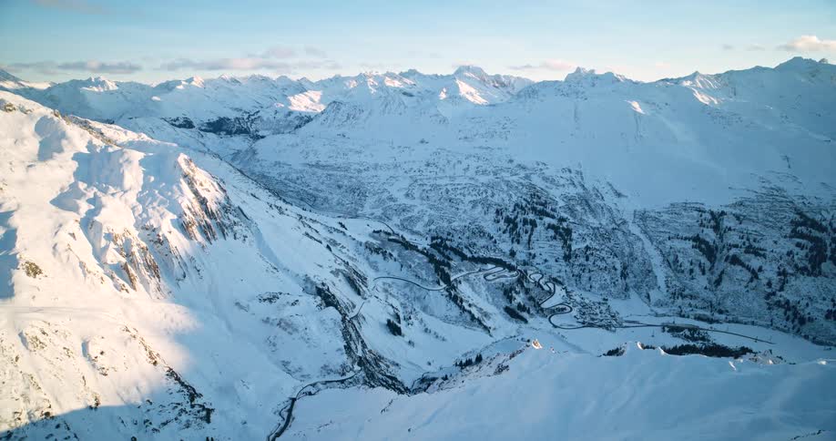 A winding road snakes through a valley surrounded by a majestic snow covered mountain range
