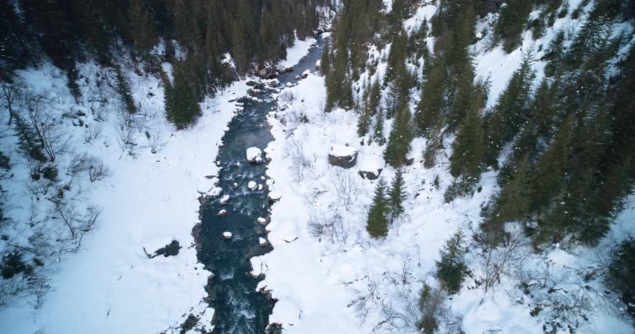 Stream flows between snow covered forested mountain slopes on a winter day