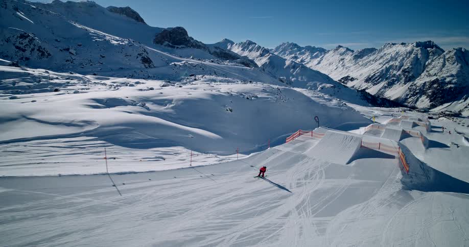 Highangle shot of a skier performing a trick on a jumping ramp in a snowpark in front of a mountain range