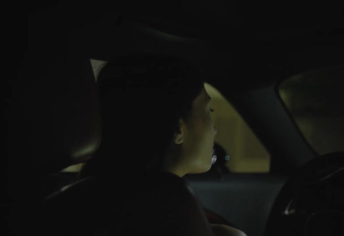 A woman is filmed from the back seat as she drives a car at night