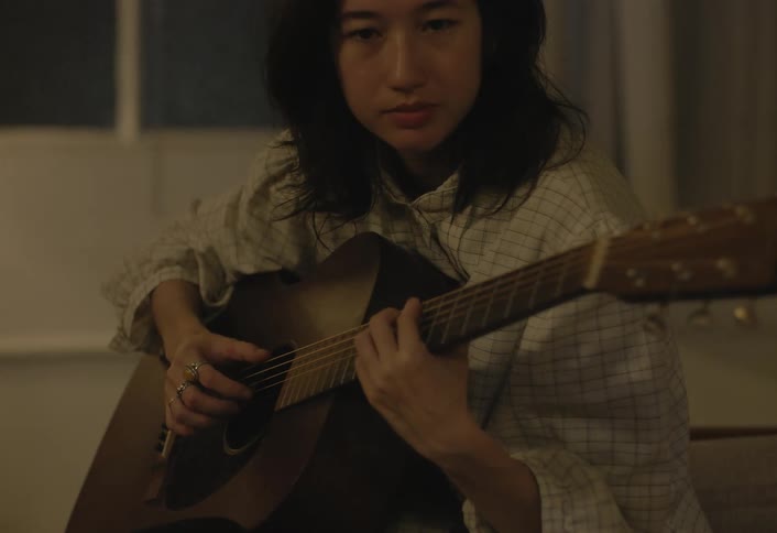 Woman plays guitar in a cozy room under soft lighting