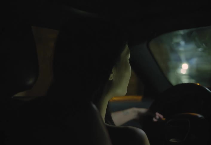 Young woman drives a car through town in traffic at night