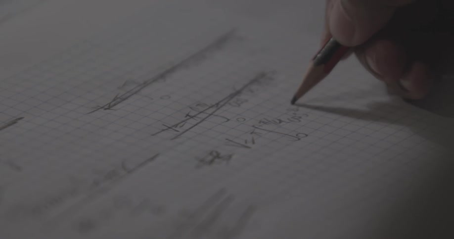 Person writes equations on a piece of graph paper with a pencil