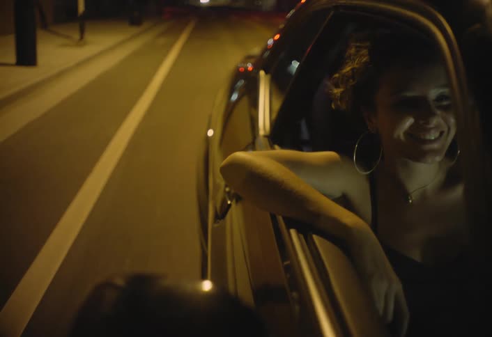 Female passenger smiles while riding in a car passing through the city at night