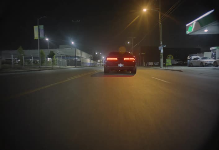 Sports car drives down a lit street at night near a gas station