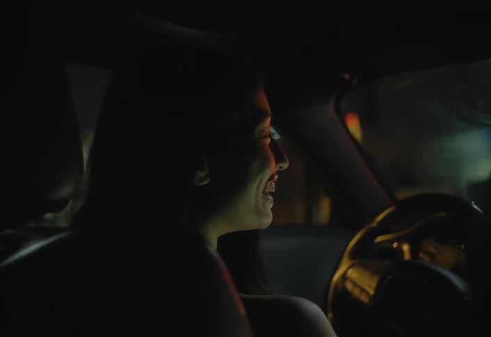 Young woman drives a car through town at night moving to the music