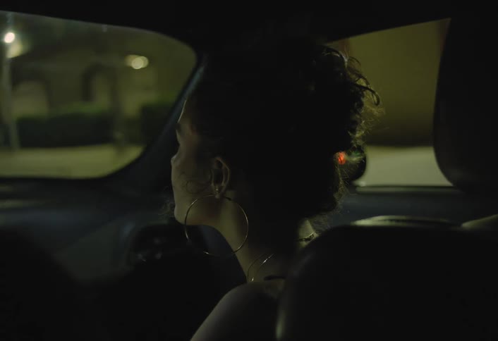 Woman sitting in the passenger seat of a vehicle looks around as the car moves along city streets at night