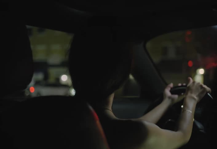 A young asian woman smiles while driving her car on a city street at night