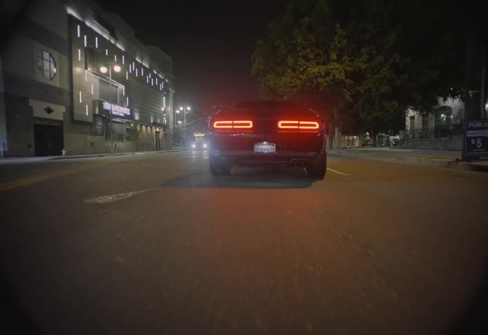 Tail lights glow in the darkness as a car moves into traffic on the road