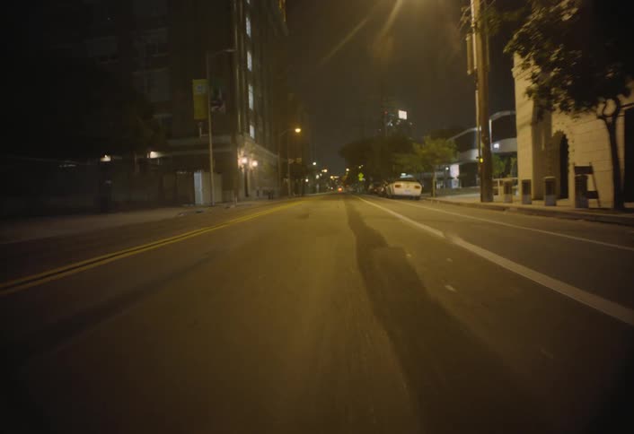 The surface of an asphalt street with some yellow streetlights on either side