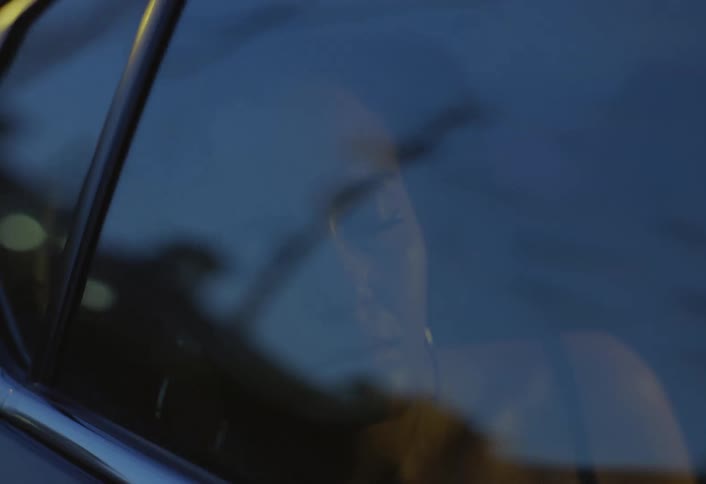 This closeup shot focuses on a woman inside a car at night resting her head near the windowthe moving lights of the city street create reflections on the glass briefly illuminating her thoughtful or tired expression