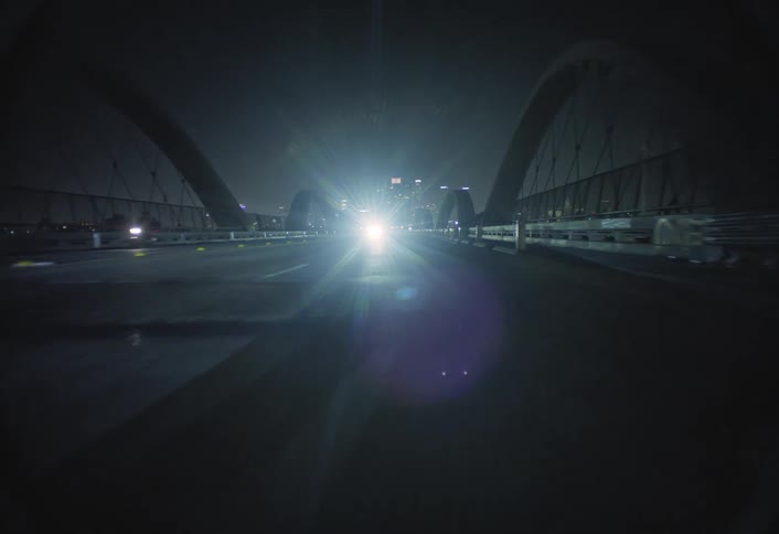 A car drives over a bridge toward a city skyline at night