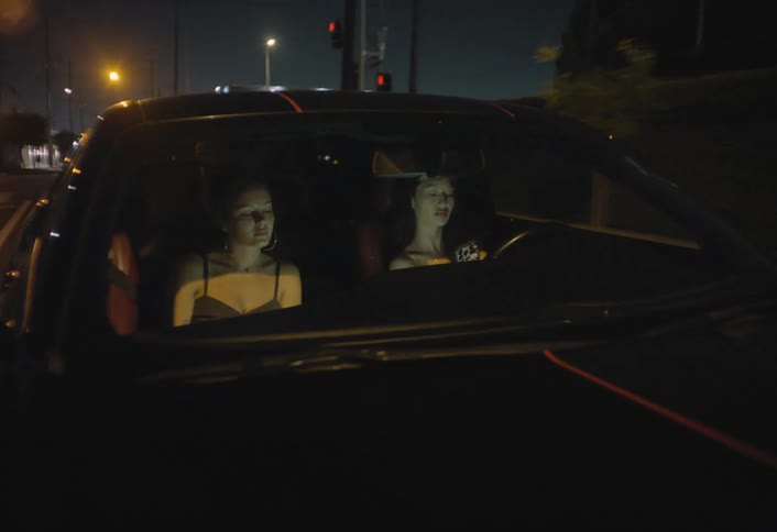 Two female adult friends driving around a city in a car at night