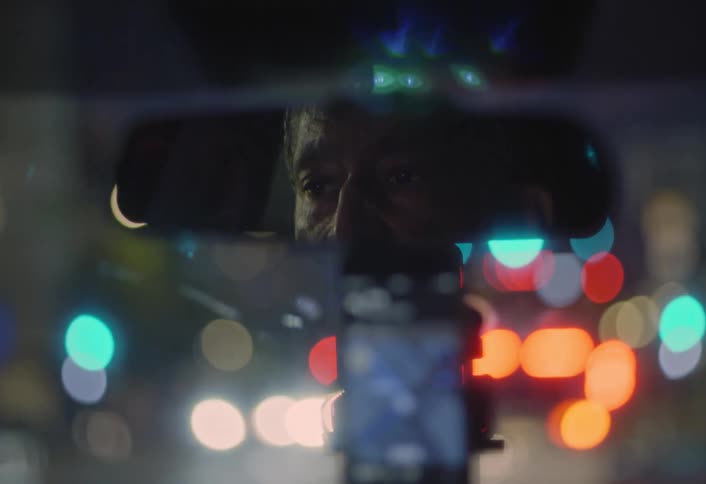 Driver is reflected in the rearview mirror amid city lights at night